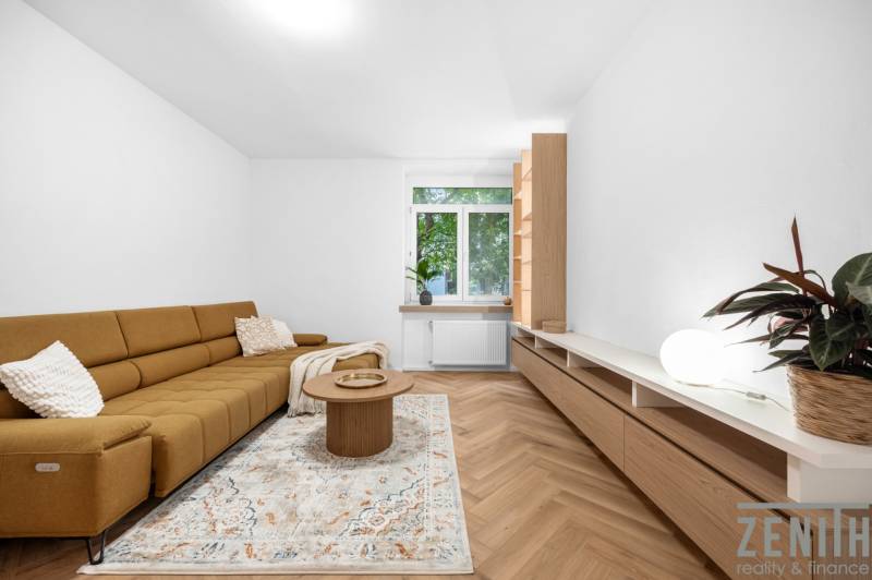 Wohnzimmer in einer 3-Zimmer-Wohnung mit braunem Sofa, Tisch und großem Fenster.