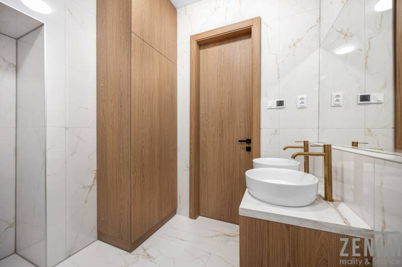 Ein Badezimmer mit zwei Waschbecken, Holzschränken und Marmorfliesen in einer 3-Zimmer-Wohnung.