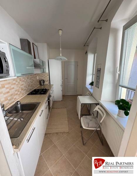Küche in einer 2-Zimmer-Wohnung mit weißen Schränken und Fenstern mit Rollläden.