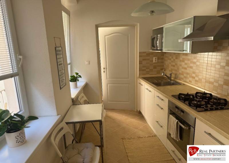 Küche in einer 2-Zimmer-Wohnung mit hellen Möbeln, Geräten und Esstisch.