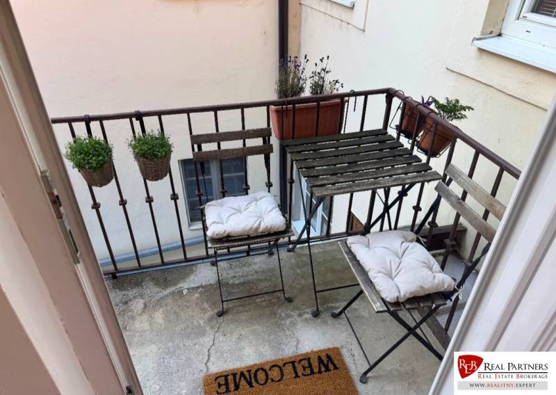 Balkon einer 2-Zimmer-Wohnung mit Metallmöbeln und Blumentöpfen.