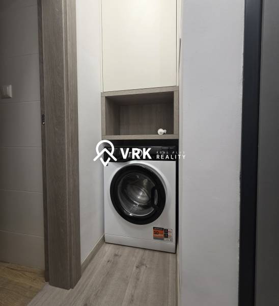 Waschmaschine in einem engen Raum einer Zweizimmerwohnung mit Holzverkleidung und Stauraum.