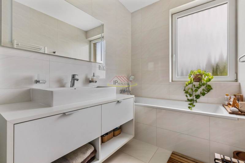 Badezimmer mit Waschbecken und Badewanne in einer 4-Zimmer-Wohnung, mit Fenster und Pflanze.