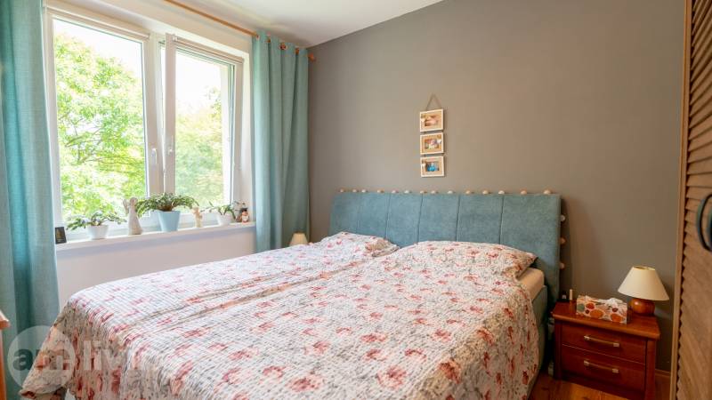Schlafzimmer mit Bett, Vorhang in einer 3-Zimmer-Wohnung und einem Nachttisch aus Holz.