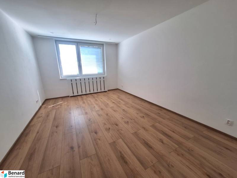 Ein leerer Raum mit Holzboden und einem großen Fenster in einer Zweizimmerwohnung.
