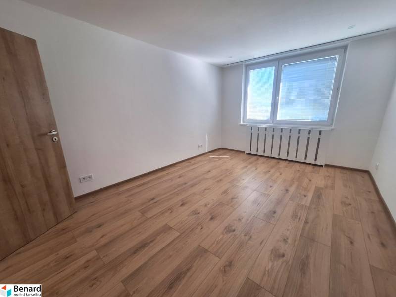 Ein geräumiges Zimmer mit Holzboden und einem großen Fenster in einer 2-Zimmer-Wohnung.