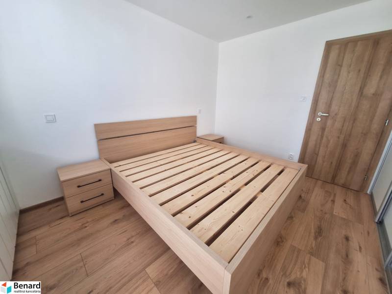 Schlafzimmer mit einem Holzbett in einer 2-Zimmer-Wohnung, ohne Matratze und mit einem Nachttisch.