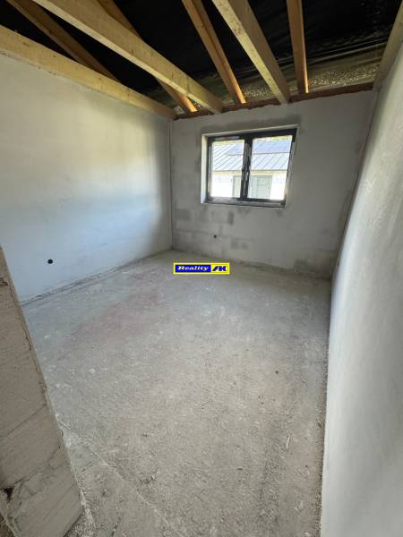 Unvollendeter Raum in einem Einfamilienhaus mit Fenster und freiliegenden Dachbalken.