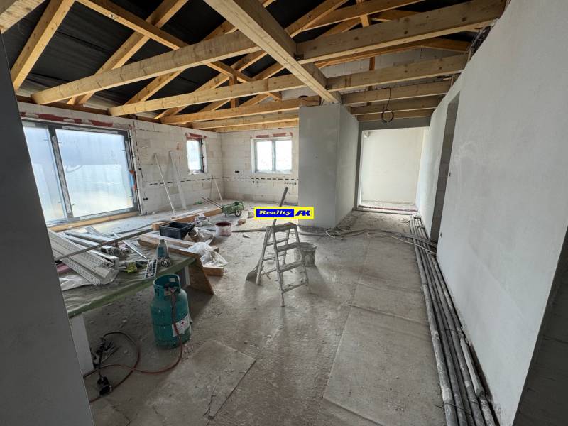 Bau in einem Einfamilienhaus mit freiliegenden Trägern und Baumaterial auf dem Boden.