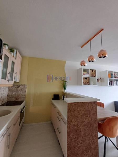 Küche in einer 2-Zimmer-Wohnung mit hängenden Leuchten und einem Holztisch.