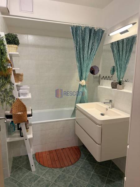 Badezimmer mit Badewanne, grünem Vorhang und Waschbecken in einer 2-Zimmer-Wohnung.
