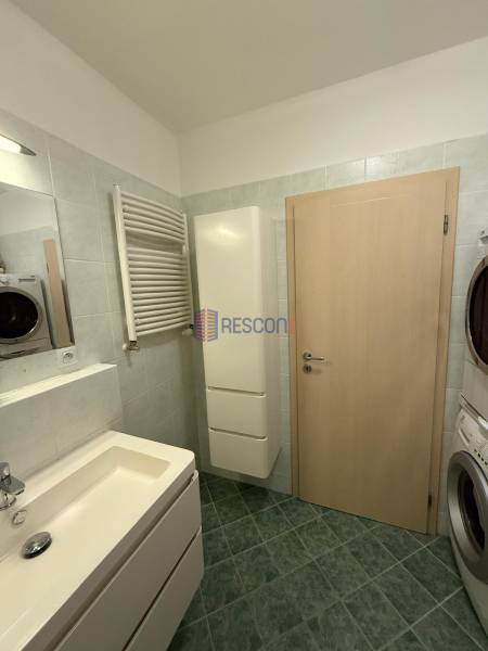 Badezimmer in einer 2-Zimmer-Wohnung mit Waschbecken, Waschmaschine und grünem Boden.