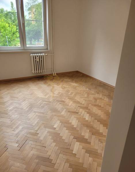 Ein Zimmer in einer 3-Zimmer-Wohnung mit Holzböden, großes Fenster, Heizkörper darunter.