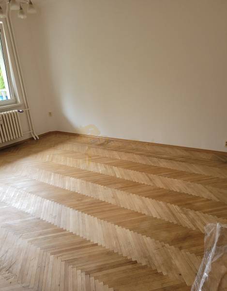 Ein leerer Raum in einer 3-Zimmer-Wohnung mit Parkettboden und einem Fenster.