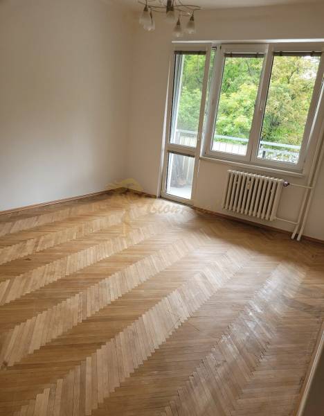Ein Zimmer in einer 3-Zimmer-Wohnung mit Holzboden und Balkontüren.