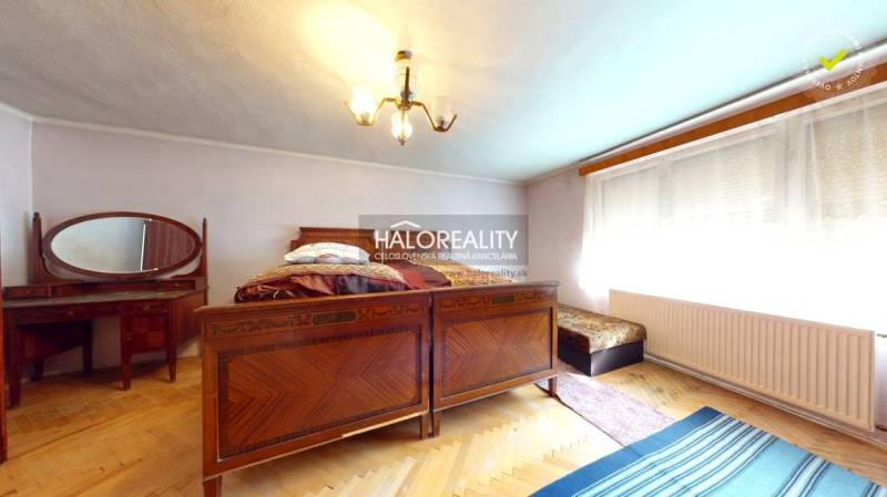 Das Innere der Hütte mit einem Holzbett, einem Kachelofen und einem Teppich.