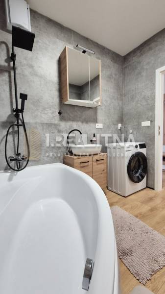 Ein Badezimmer mit grauen Fliesen, einer Badewanne, einer Waschmaschine und einem Waschbecken in einer Vierzimmerwohnung.