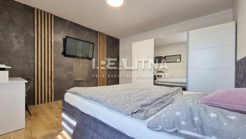 Schlafzimmer in einer 4-Zimmer-Wohnung mit einem bequemen Bett, einem Kleiderschrank und einem Fernseher.