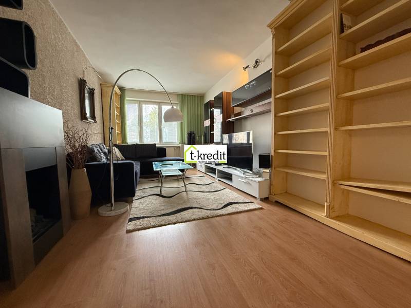 Wohnzimmer einer Zweizimmerwohnung mit schwarzem Sofa, Teppich und Holzregalen.