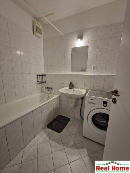 Badezimmer mit Badewanne und Waschmaschine in einer 2-Zimmer-Wohnung, Fliesenboden und weiße Fliesen.
