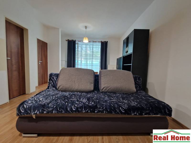 Wohnbereich, Sofa, Kissen, dunkle Möbel, Vorhänge, heller Boden, Einzimmerwohnung.