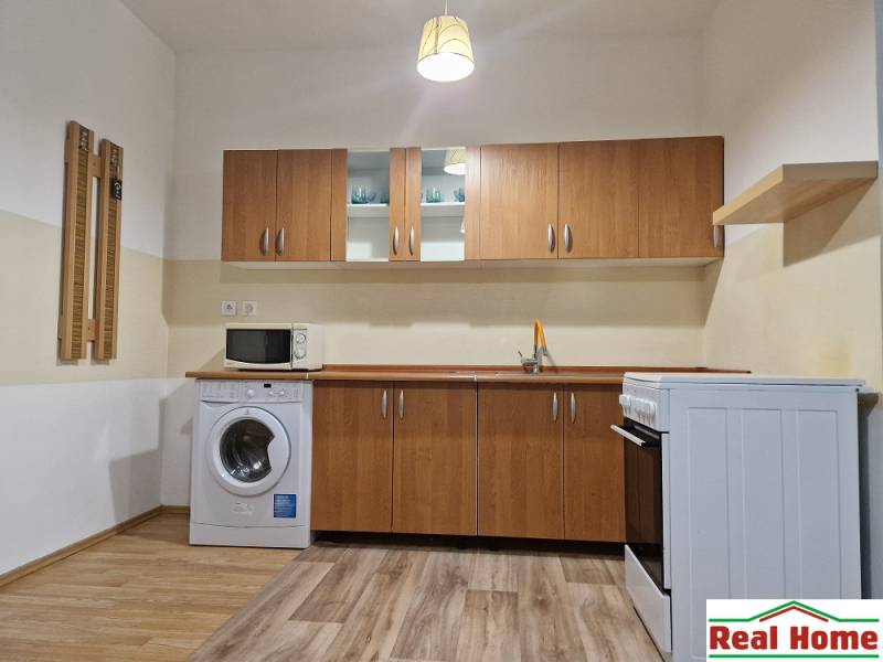 Küche in einer Einzimmerwohnung mit Herd, Mikrowelle und Waschmaschine, Holzschränke.