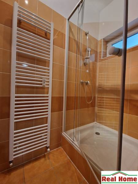 Duschkabine im Badezimmer einer Einzimmerwohnung mit Fliesen und Heizkörper.