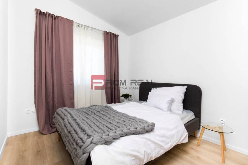 Schlafzimmer in einer 3-Zimmer-Wohnung mit Bett, grauer Decke und Nachttisch.