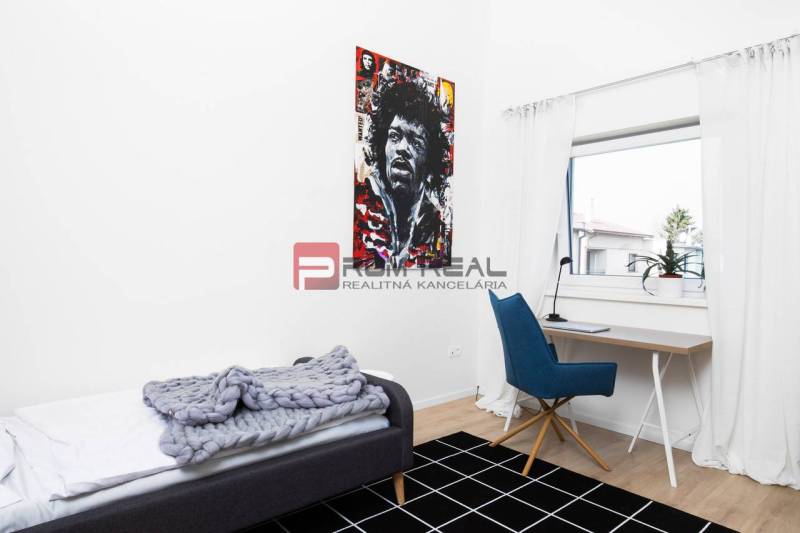 Einfaches Zimmer mit Tisch, Stuhl, Bett und einem bunten Bild an der Wand in einer 3-Zimmer-Wohnung.
