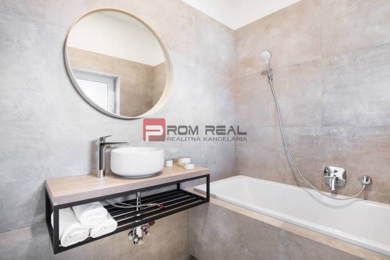 Badezimmer mit Waschbecken, Badewanne und rundem Spiegel in einer 3-Zimmer-Wohnung.
