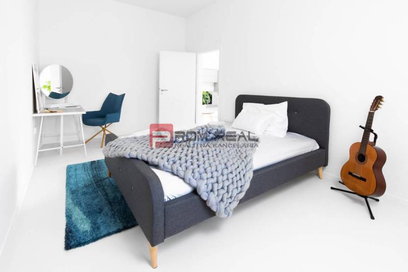 Einfaches Schlafzimmer mit Bett, Tisch, Stuhl und Gitarre in einer 3-Zimmer-Wohnung.