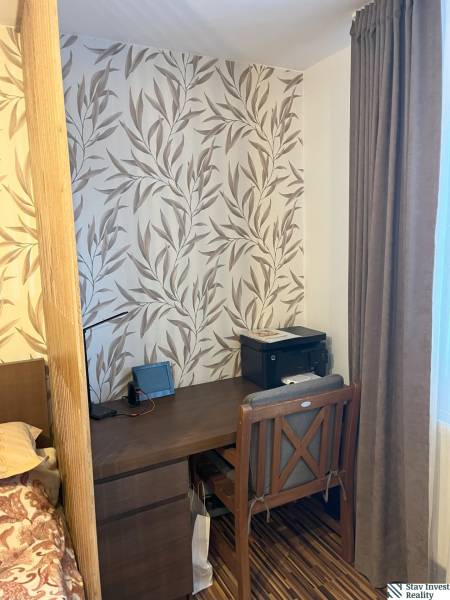 Ein Arbeitsbereich in einer 2-Zimmer-Wohnung mit einer Tapete mit Blattmuster und dunklen Möbeln.