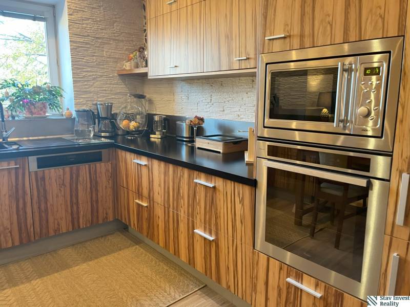 Küche mit Holzschränken, eingebautem Ofen und Fenster in einer Zweizimmerwohnung.