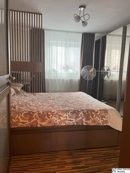 Schlafzimmer in einer Zweizimmerwohnung mit Doppelbett, Lampe und Fenstern mit schweren Vorhängen.