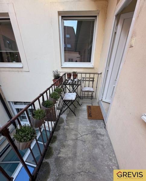 Ein schmaler Balkon mit Metallgeländer, Stühlen und Blumentöpfen in einer Zweizimmerwohnung.