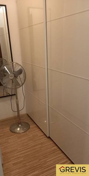 Ein Kleiderschrank in einer 2-Zimmer-Wohnung mit weißen Schiebetüren und einem Standventilator.