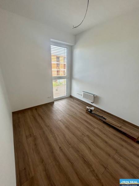 Ein leerer Raum mit Laminatboden und einem großen Fenster in einer 3-Zimmer-Wohnung.