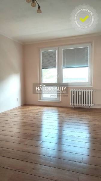 Ein Zimmer mit Holzboden in einer 4-Zimmer-Wohnung, ausgestattet mit einem Heizkörper und Fenstern mit Jalousien.