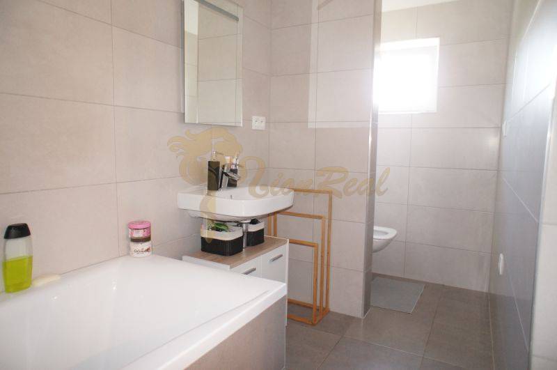 Badezimmer in einem Einfamilienhaus mit Badewanne, Waschbecken, Duschkabine und großformatigen Fliesen.
