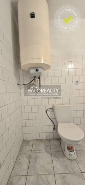 Ein Badezimmer in einem Einfamilienhaus mit Toilette und Boiler, gefliest mit weißen Fliesen.