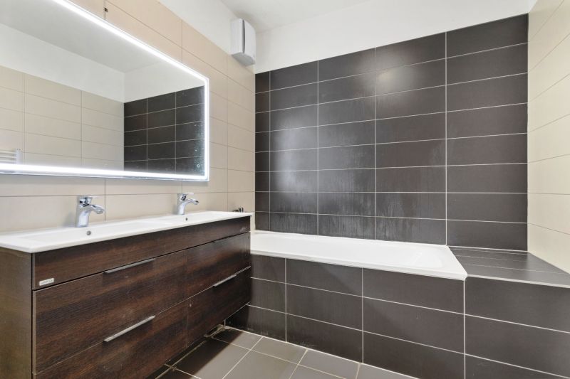 Badezimmer mit Doppelwaschbecken, Badewanne und grauen Fliesen in der Vukovarská-Straße in einer 3-Zimmer-Wohnung.