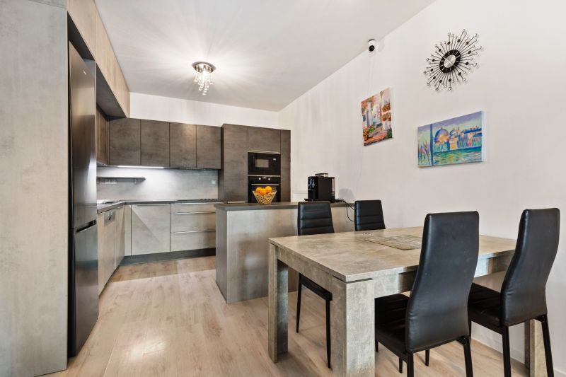 Küche in einer 3-Zimmer-Wohnung in der Vukovarská-Straße; graue Schränke, Esstisch, Dekorationen.