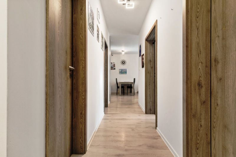 Ein Flur mit Holztüren, hellem Boden, Bildern an den Wänden neben einer 3-Zimmer-Wohnung.