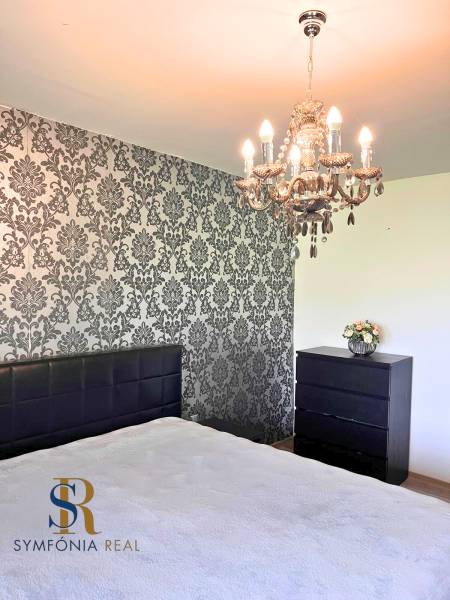 Schlafzimmer mit Kronleuchter und Tapetenwand in einem Einfamilienhaus. Boden mit Holzdekor.