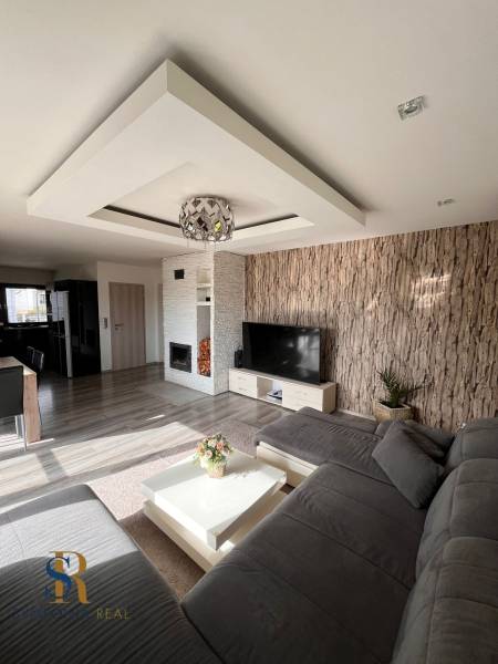 Wohnzimmer in einem Einfamilienhaus mit Sofa, Fernseher und Kamin, Boden mit Holzdekor.