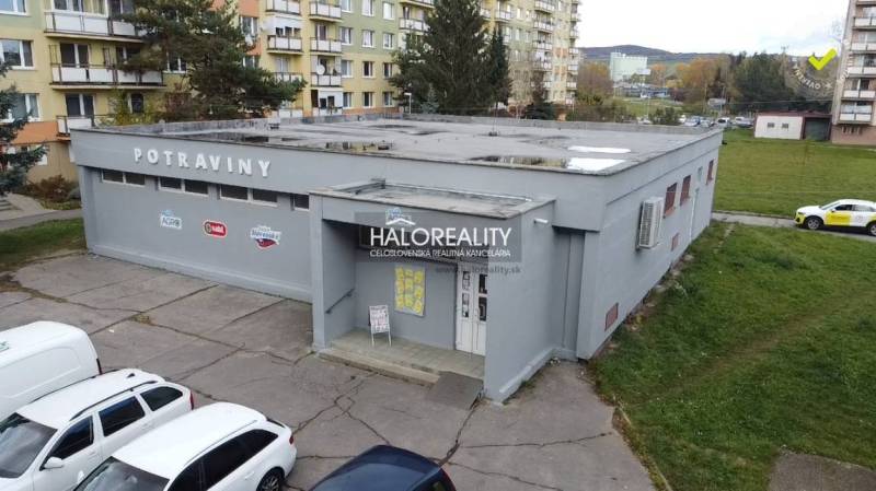 Ein Geschäftsgebäude in Rimavská Sobota, umgeben von Plattenbauten und geparkten Autos.