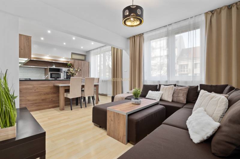 Wohnzimmer mit Holzboden in einer Zweizimmerwohnung mit Ecksofa und Küche.