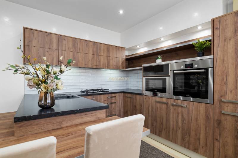 Küche in einer 2-Zimmer-Wohnung, Holzdekor, weiße Fliesen, eingebaute Geräte.