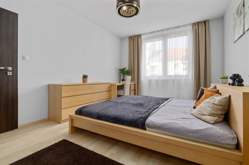 Schlafzimmer mit Bett und Kommode in einer 2-Zimmer-Wohnung, Boden mit Holzdekor.