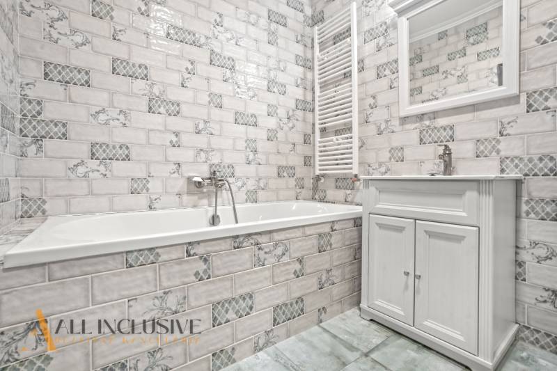 Badezimmer in der Ausführung einer 2-Zimmer-Wohnung mit weißen Fliesen und einer Badewanne.